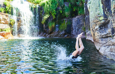 Young boy jumps into the water of the natural pool with waterfall
