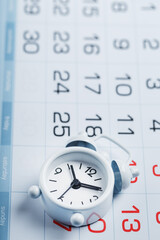 Fototapeta premium The white alarm clock is on the calendar with dates
