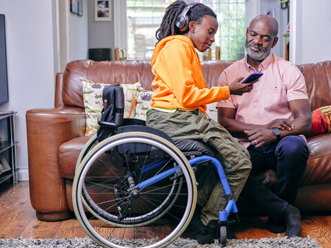 Girl in wheelchair and grandfather using smart phone