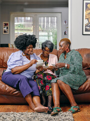 Women and senior mother sitting on sofa and looking at photos
