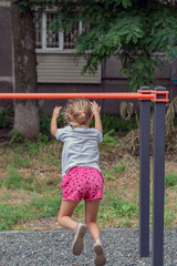 an active child, a girl of 6-7 years old plays on the sports ground, hangs on the uneven bars