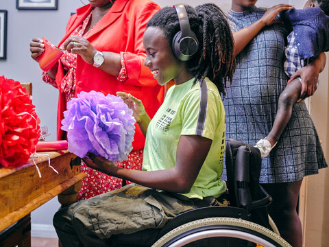 Smiling girl in wheelchair making paper decorations with family