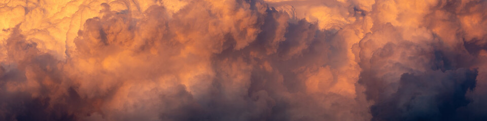 a wide panoramic view of an orange-purple stormy sunset sky with cumulus clouds. atristic moody image for dramatic design or decoration