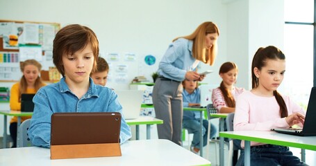 Close up portrait of Caucasian teen schoolboy typing on tablet, exam test at computer science class.