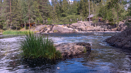 stormy mountain river with a waterfall and tourists on a pedestrian suspension bridge in Karelia, Russia