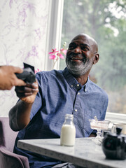 UK, SmilingÊman paying with smart phone at cafe table