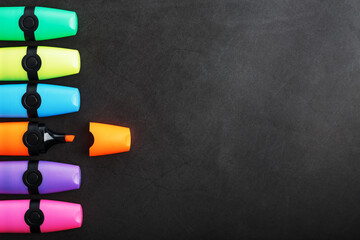 Multi-colored markers in a row on a black background, top view.
