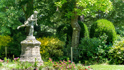 Statue of an ancient person slender on one foot, surrounded by lush plants and trees	