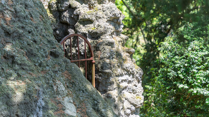 Red metal gate, arched top, between the rocks, closing the access to a waterfall