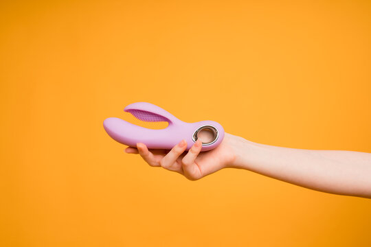 Sex gadgets and masturbation devices. Pink dildo in woman's hand on orange background. sex toys
