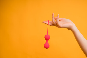 A woman's hand with vaginal Kegel balls or a sex toy for adults to achieve a female orgasm on a yellow background