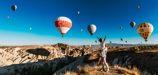 A happy couple among balloons in Cappadocia. A couple in love against the background of flying balloons in Cappadocia. Travel to Turkey. Balloons in the sky, panorama. Wedding trip. Honeymoon trip