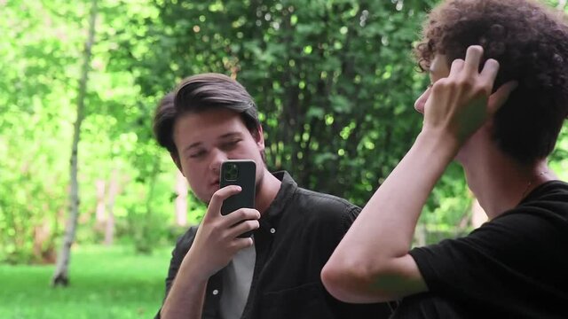 A guy takes pictures on the phone of another guy in nature in the summer