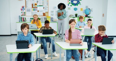 African American pretty young woman teacher at work at school walks in class using tablet at...