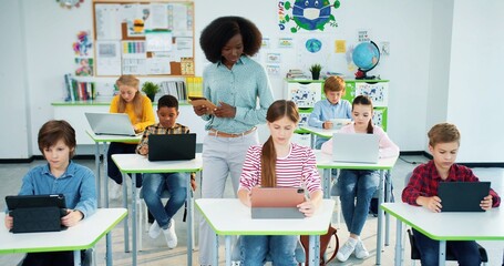 Multi-ethnic diverse junior students studying at school using laptop and tablets, technology,...