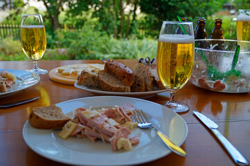 a traditional, rustic and hearty German dinner at a beer garden with a couple of beers, a German or also Swiss sausage salad (Wurstsalat) with cheese and onions and a basket of bread