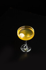 Glass with yellow lemon cocktail on the bar on a black background. the drinks is decorated with flower