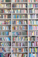 Blurred image of a library with bookcases. Many different books on the shelves. Large selection of books in a bookcase. Blurred background. - obrazy, fototapety, plakaty
