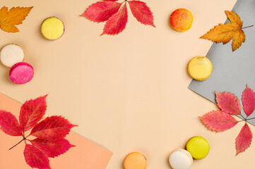 Autumn frame from leaves and macarons on colored pastel paper. Copy space. Food art.  Top view