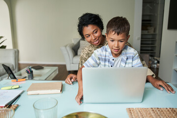 Black mother looking on her son with laptop