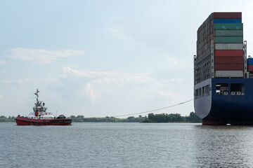 the tug accompanies a large container cargo ship from port