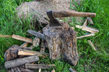 Old ax with pile of chopped firewood and a deck for chopping wood on the background of green grass 
