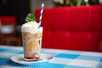 Iced caramel latte coffee in a tall glass with white chocolate syrup, whipped cream and mint leaf.