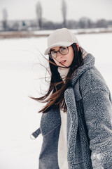 Portrait of an attractive girl dressed in stylish winter clothes. Woman posing for a photo on a snow-covered and icy lake in a local park