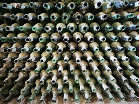 Many green and empty wine bottles, forgotten in a wine cellar. Bottles are cover with dust and spider webs. Old bottles are opened. Time goes by. 