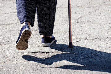 Woman walking with a cane on a street, female legs on sidewalk. Concept of disability, limping person, diseases of the spine, old people - obrazy, fototapety, plakaty