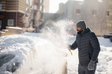 A young man cleans his car after a snowfall on a sunny, frosty day.