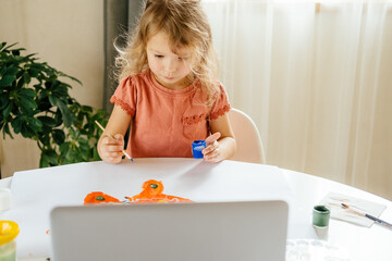 Young cute girl spending a time drawing using online lessons on laptop. Distance learning, online education.