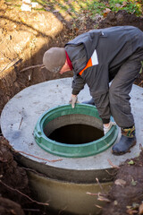 A worker installs a sewer manhole on a septic tank made of concrete rings. Construction of sewage disposal systems for private houses.