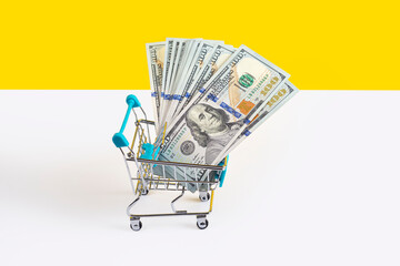 Toy supermarket cart or shopping trolley full of money isolated on yellow and white background. Money loan or sale concept. Banner with copy space.