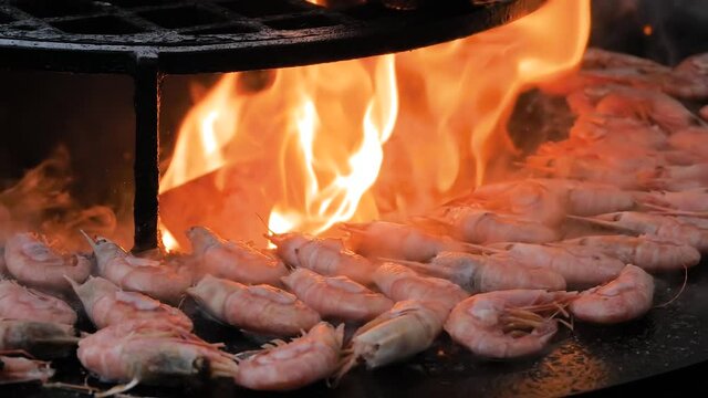 Super slow motion: chef grilling fresh red king prawns on brazier with hot flame at summer local food market - close up. Outdoor cooking, barbecue, gastronomy, seafood, cookery, street food concept