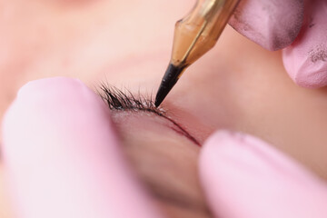 Permanent makeup artist making eyelid tattoo for client in beauty salon closeup