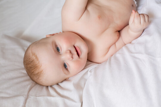 a cute baby is lying in diapers in a bed with white cotton bed linen. High quality photo