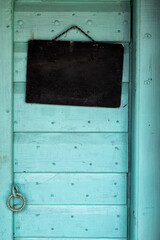 Ancient, old, wooden teal door with a empty blackboard