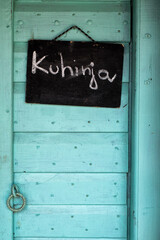 Ancient, old, wooden teal door with Kuhinja blackboard sign