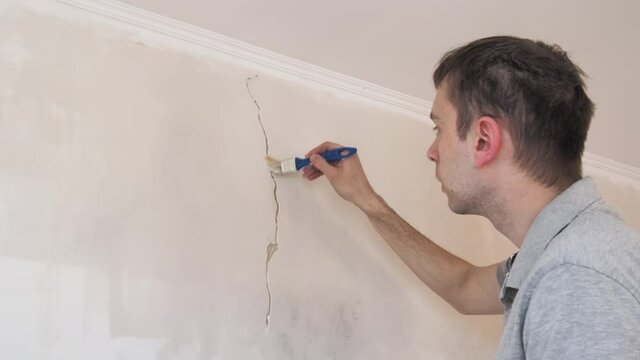 Construction man worker repairing a crack wall of a home, plastering cement on wall. Builder applying white cement to a crack in a wall with a putty knife 