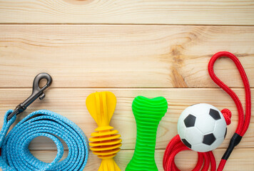 Different multicolored pet care accessories: ring, bones, balls on natural wooden background. Rubber and textile accessories for dogs. Top view, flat lay. Copy space	
