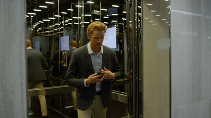 Fototapeta na wymiar Serious businessman using smartphone in lift. Manager typing on mobile phone