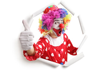 Cheerful clown peeking through a paper hole and gesturing thumbs up