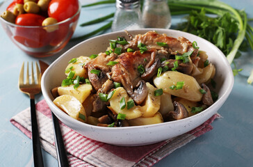 Rabbit meat with potatoes and mushrooms in a light plate on a light blue background.