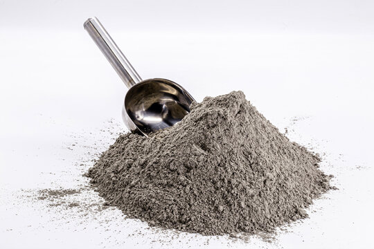 Cement powder pile on isolated white background with metal measuring spoon.