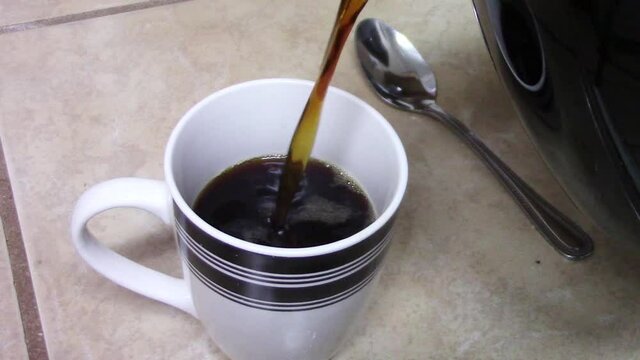 Close-up of pouring a strong black cup of coffee in a white and black striped cup