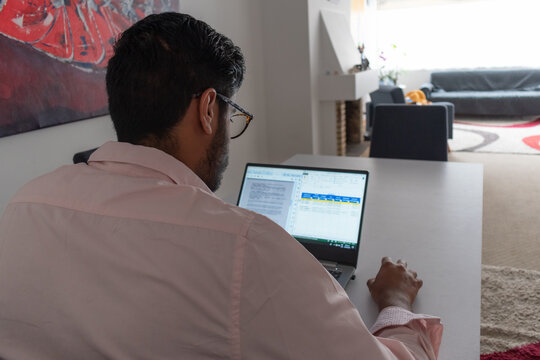 1 hombre moreno con barba y gafas teletrabajando desde casa en su laptop 
