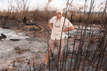 Man from the environment inspecting the remains of a brush fire at an illegal trash dump in Granja...
