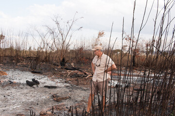 Man from the environment inspecting the remains of a brush fire at an illegal trash dump in Granja...