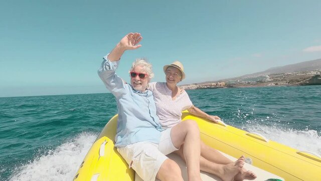 Beautiful and cute couple of seniors or old people in the middle of the sea driving and discovering new places with small boat. Mature woman holding a phone and taking a selfie with hew husband
